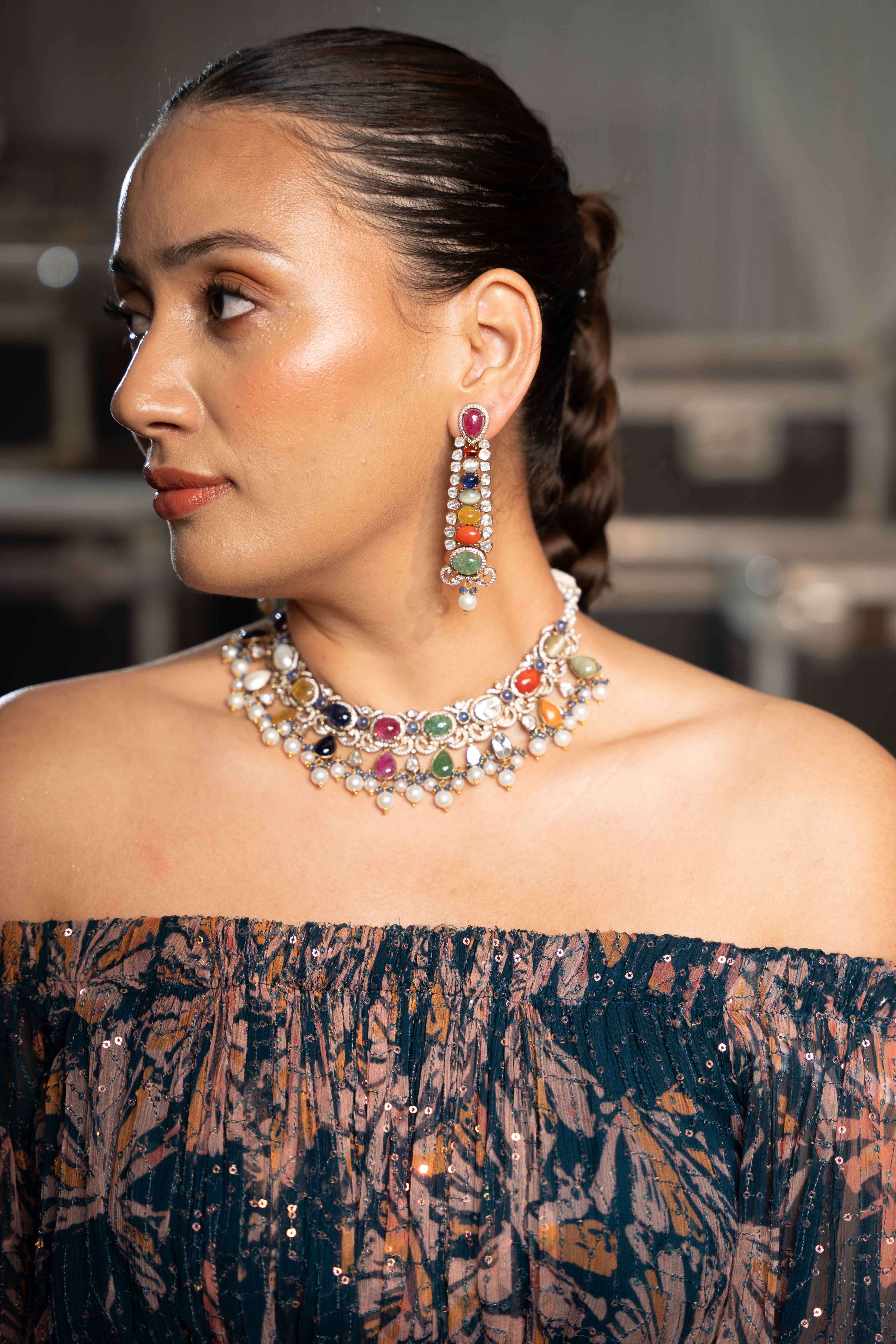 Woman in black dress with layered gold necklaces against coastal backdrop